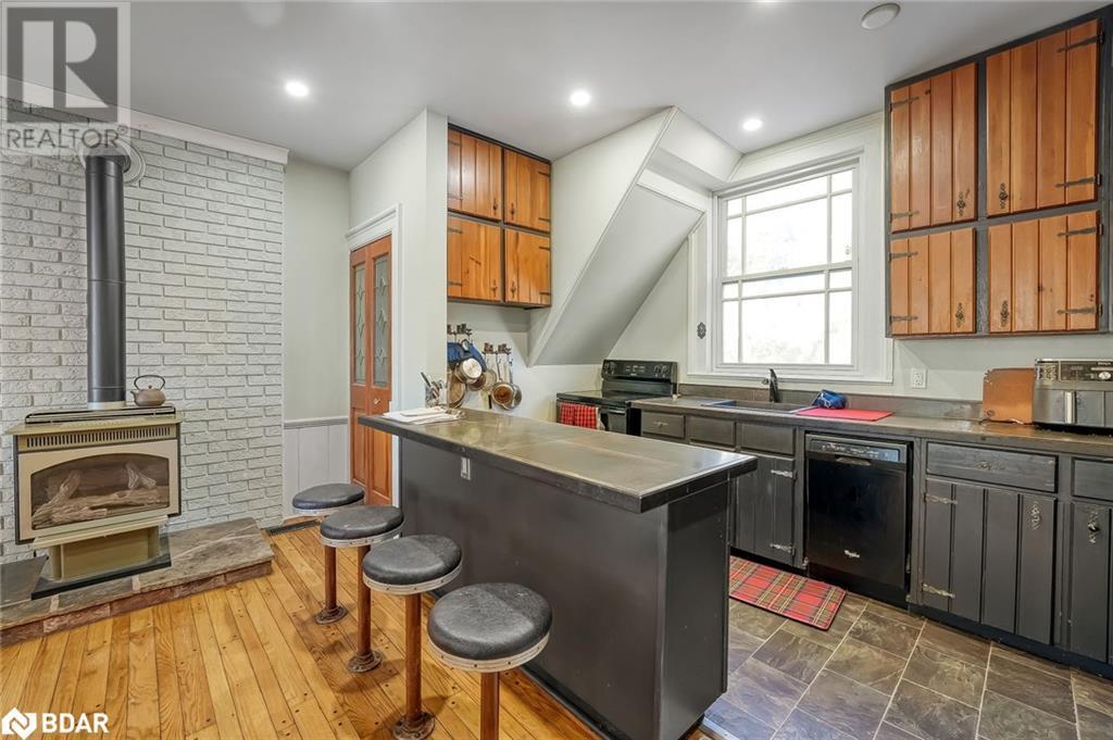 Kitchen featuring a wood stove, dark countertops, a peninsula, a kitchen bar, and black appliances - 7369 5Th Sideroad Side Road, Adjala-Tosorontio, ON
