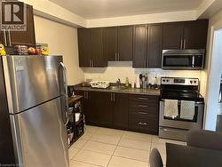 Kitchen featuring stainless steel appliances, dark countertops, light tile patterned flooring, dark brown cabinets, and decorative backsplash -