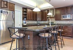 Kitchen with stainless steel appliances, dark brown cabinetry, hanging light fixtures, a kitchen breakfast bar, and wall chimney range hood -