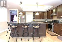 Kitchen with wall chimney range hood, pendant lighting, an island with sink, and stainless steel appliances -