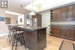 Kitchen featuring dark brown cabinetry, a center island with sink, and stainless steel fridge -