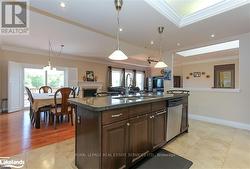 Kitchen featuring ornamental molding, a center island with sink, light wood-type flooring, dark brown cabinetry, and dishwasher -