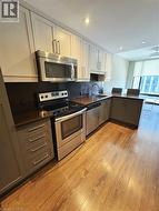 Kitchen featuring appliances with stainless steel finishes, a sink, light wood-style flooring, dark countertops, and a peninsula -