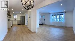 Kitchen with light wood-style floors, wall chimney range hood, appliances with stainless steel finishes, a chandelier, and white cabinets -