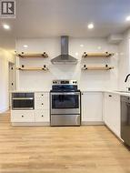 Kitchen featuring stainless steel appliances, wall chimney exhaust hood, white cabinetry, open shelves, and recessed lighting -