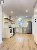 Kitchen featuring open shelves, appliances with stainless steel finishes, backsplash, wall chimney range hood, and recessed lighting -