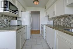 Kitchen with white appliances, white cabinets, backsplash, and light tile patterned floors -