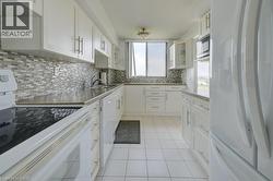 Kitchen featuring white appliances, light tile patterned floors, white cabinets, and decorative backsplash -