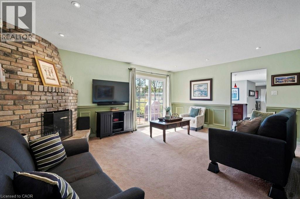 Living room with a decorative wall, a brick fireplace, a textured ceiling, carpet flooring, and wainscoting - 3 Meadowbrook Court, St. George, ON - Indoor Photo Showing Living Room With Fireplace