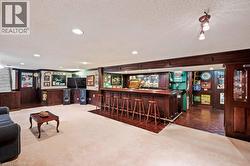 Indoor dry bar with a textured ceiling, dark colored carpet, recessed lighting, ornamental molding, and dark brown cabinets -