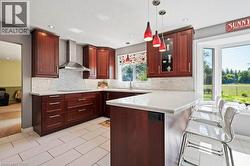 Kitchen featuring a breakfast bar area, decorative backsplash, a peninsula, wall chimney exhaust hood, and recessed lighting -