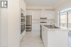 Kitchen featuring white cabinets, a kitchen island with sink, stainless steel appliances, light marble finish floors, and light countertops -