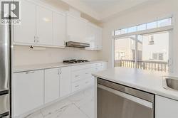 Kitchen with appliances with stainless steel finishes, white cabinetry, light countertops, light marble finish flooring, and range hood -