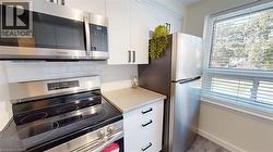 Kitchen featuring stainless steel appliances, white cabinets, backsplash, and wood finished floors -