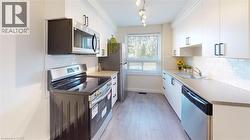 Kitchen with stainless steel appliances, light wood-style flooring, tasteful backsplash, and white cabinets -