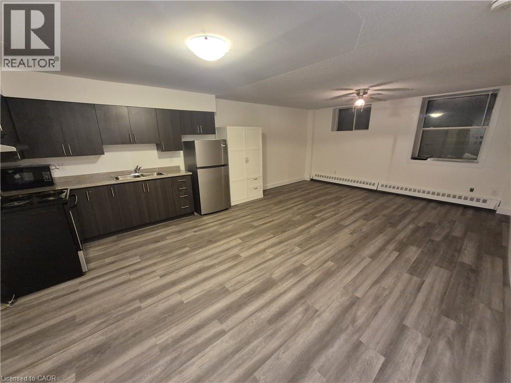 Kitchen with black appliances, light wood finished floors, light countertops, a baseboard heating unit, and ceiling fan - 27 Bridge Street Unit# 107, Brantford, ON - Indoor Photo Showing Kitchen With Double Sink