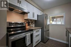 Kitchen featuring appliances with stainless steel finishes, white cabinetry, under cabinet range hood, tasteful backsplash, and dark wood-style floors -
