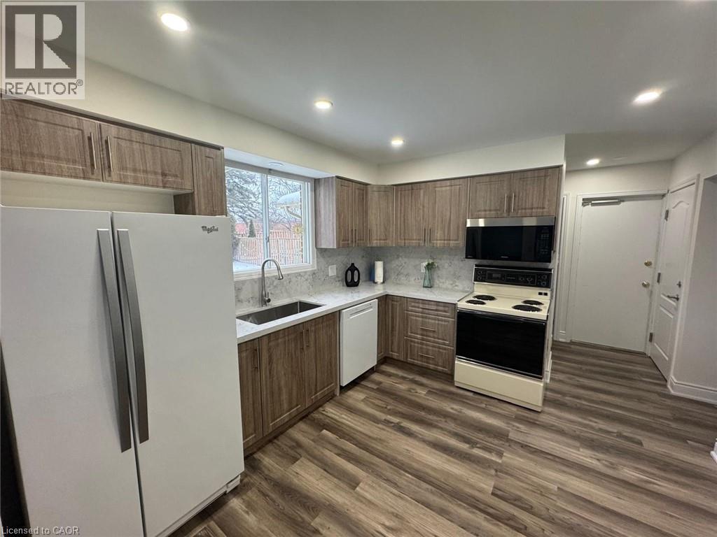Kitchen featuring white appliances, dark wood finished floors, tasteful backsplash, recessed lighting, and brown cabinets - 389 Dunvegan Drive, Waterloo, ON - Indoor Photo Showing Kitchen