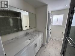 Bathroom featuring vanity, a marble finish shower, light marble finish floors, and stacked washer and clothes dryer -