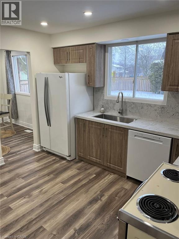 Kitchen featuring white appliances, brown cabinets, dark wood finished floors, backsplash, and recessed lighting - 389 Dunvegan Drive, Waterloo, ON - Indoor Photo Showing Kitchen With Double Sink