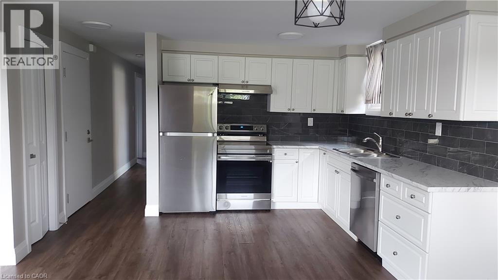 Kitchen with appliances with stainless steel finishes, decorative backsplash, white cabinets, dark wood-style floors, and under cabinet range hood - 106 Chandler Drive Unit# 1, Kitchener, ON - Indoor Photo Showing Kitchen With Stainless Steel Kitchen With Double Sink