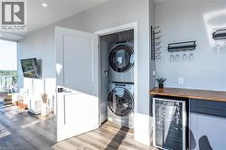 Laundry area with wine cooler, a bar, wood finished floors, stacked washing machine and dryer, and recessed lighting -