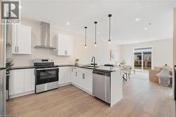 Kitchen featuring appliances with stainless steel finishes, wall chimney exhaust hood, white cabinets, hanging light fixtures, and recessed lighting -