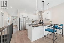 Kitchen featuring a peninsula, white cabinetry, stainless steel appliances, light wood finished floors, and wall chimney exhaust hood -