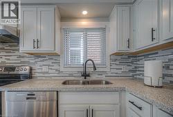 Kitchen with tasteful backsplash, stainless steel appliances, extractor fan, and white cabinetry -