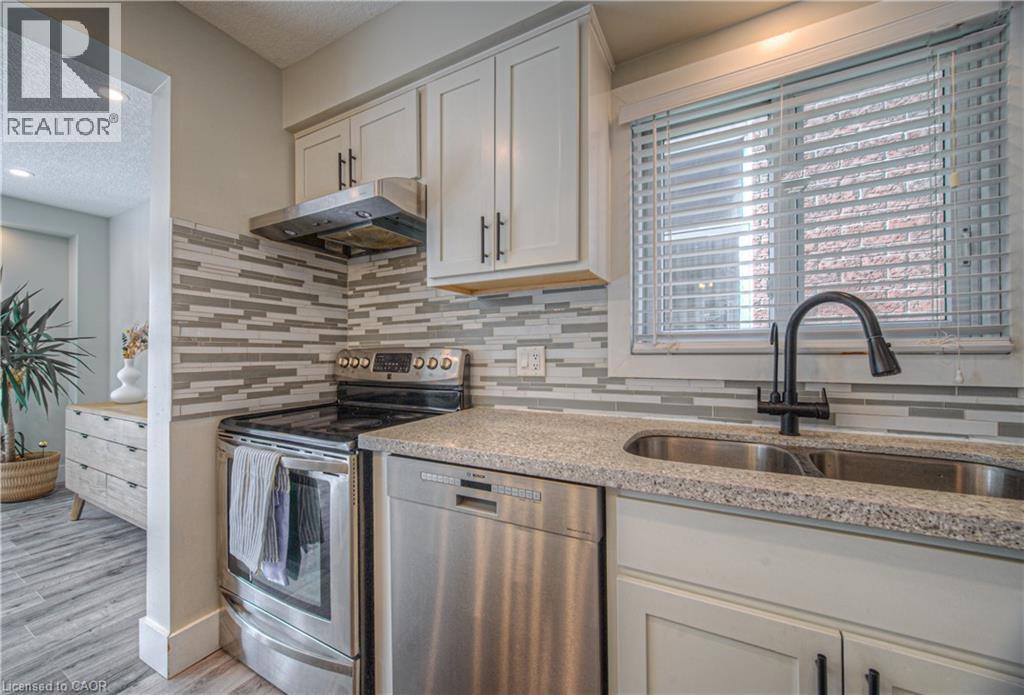 Kitchen featuring stainless steel appliances, under cabinet range hood, decorative backsplash, a textured ceiling, and light stone counters - 220 Sienna Crescent, Kitchener, ON - Indoor Photo Showing Kitchen With Double Sink