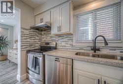 Kitchen featuring stainless steel appliances, under cabinet range hood, decorative backsplash, a textured ceiling, and light stone counters -