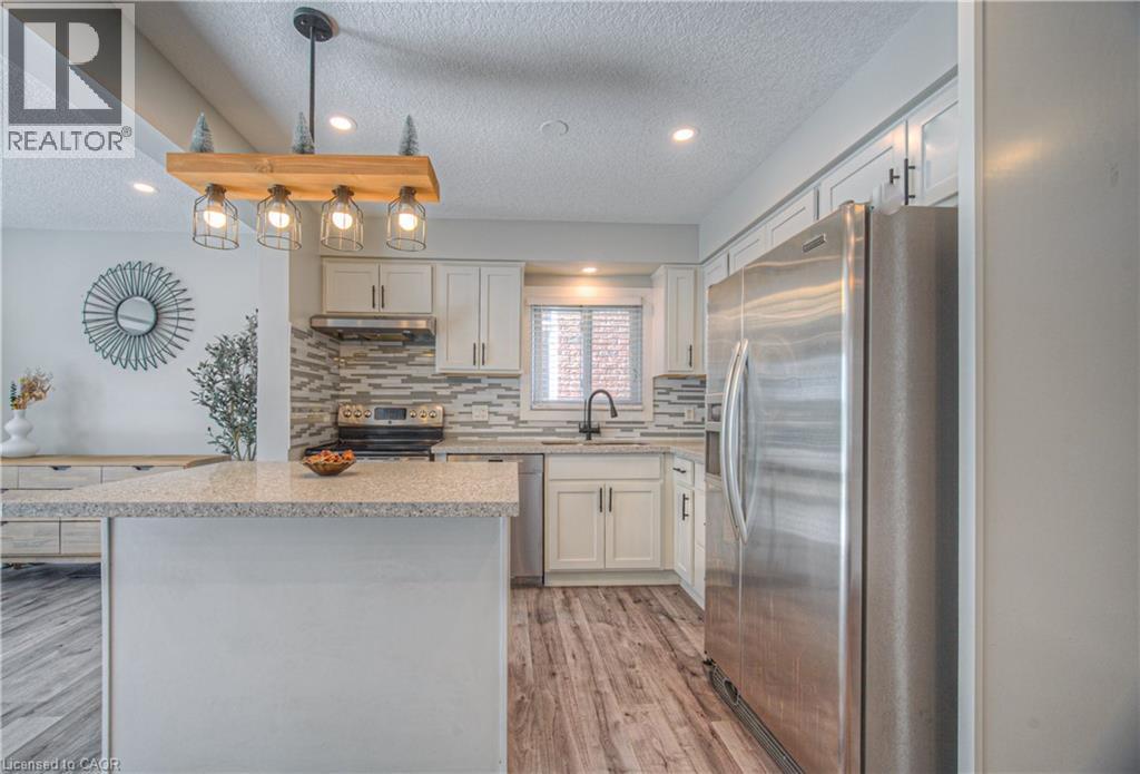 Kitchen featuring stainless steel appliances, a textured ceiling, hanging light fixtures, light wood-type flooring, and a kitchen island - 220 Sienna Crescent, Kitchener, ON - Indoor Photo Showing Kitchen With Stainless Steel Kitchen With Upgraded Kitchen