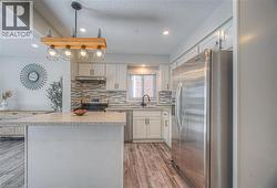 Kitchen featuring stainless steel appliances, a textured ceiling, hanging light fixtures, light wood-type flooring, and a kitchen island -