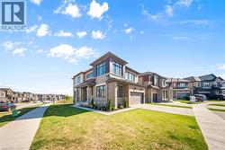 View of front of house featuring a residential view, concrete driveway, a front lawn, brick siding, and a garage -