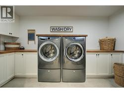 Dedicated main floor laundry room with washer and dryer on risers, custom cabinetry, a wash sink and wood inspired countertops -