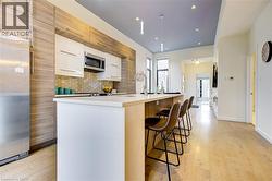 Kitchen with tasteful backsplash, white cabinets, stainless steel appliances, light wood-style floors, and a center island with sink -