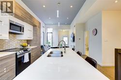 Kitchen featuring modern cabinets, white cabinetry, appliances with stainless steel finishes, decorative backsplash, and light wood-style floors -