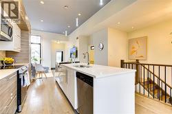 Kitchen featuring appliances with stainless steel finishes, white cabinets, light wood-style flooring, an island with sink, and light stone counters -