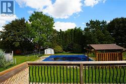View of swimming pool with a storage unit, view of scattered trees, and a fenced backyard -