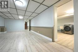 Finished below grade area with washer / dryer, light wood-style flooring, and a paneled ceiling -