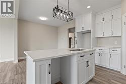 Kitchen with hanging light fixtures, a kitchen island with sink, light wood-style floors, white cabinets, and recessed lighting -