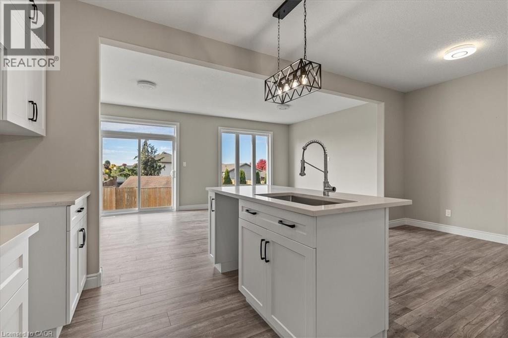 Kitchen with white cabinetry, decorative light fixtures, a kitchen island with sink, light wood-type flooring, and light stone countertops - 256 Keeso Lane, Listowel, ON - Indoor Photo Showing Other Room