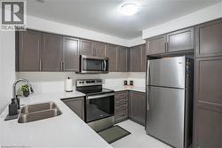 Kitchen featuring appliances with stainless steel finishes, tasteful backsplash, light tile patterned floors, dark brown cabinets, and light stone countertops -