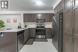 Kitchen featuring dark brown cabinets, appliances with stainless steel finishes, a peninsula, light tile patterned flooring, and tasteful backsplash -