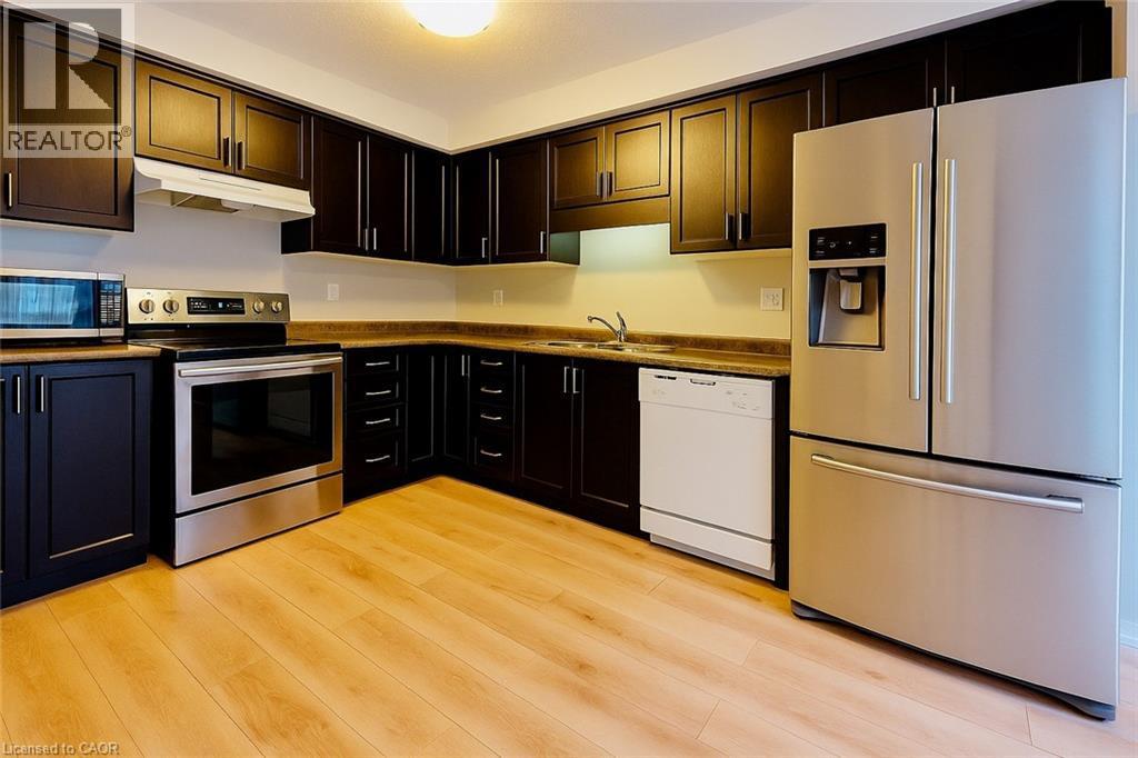 Kitchen with appliances with stainless steel finishes, under cabinet range hood, dark countertops, and light wood finished floors - 6 Upper Mercer Street Unit# B6, Kitchener, ON - Indoor Photo Showing Kitchen With Double Sink
