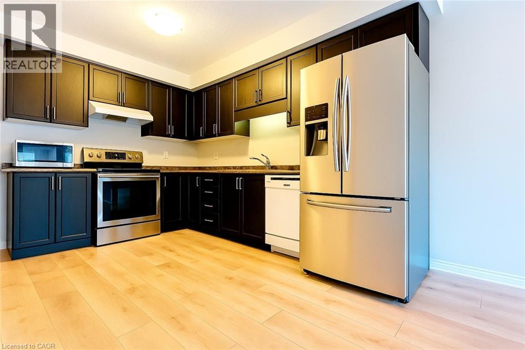 Kitchen with stainless steel appliances, dark countertops, light wood finished floors, and under cabinet range hood - 6 Upper Mercer Street Unit# B6, Kitchener, ON - Indoor Photo Showing Kitchen