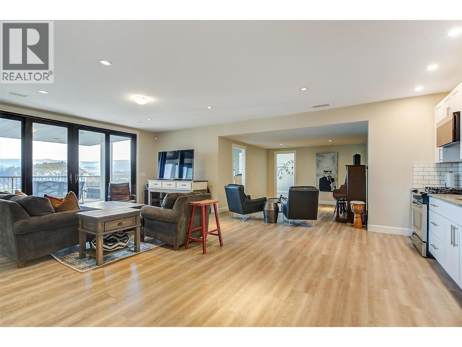 The lower level boasts vinyl plank flooring and a spacious open-concept family room, highlighted by floor-to-ceiling windows and sliding glass doors that open to the back patio and pool area. - 738 Highpointe Drive, Kelowna, BC - Indoor Photo Showing Living Room