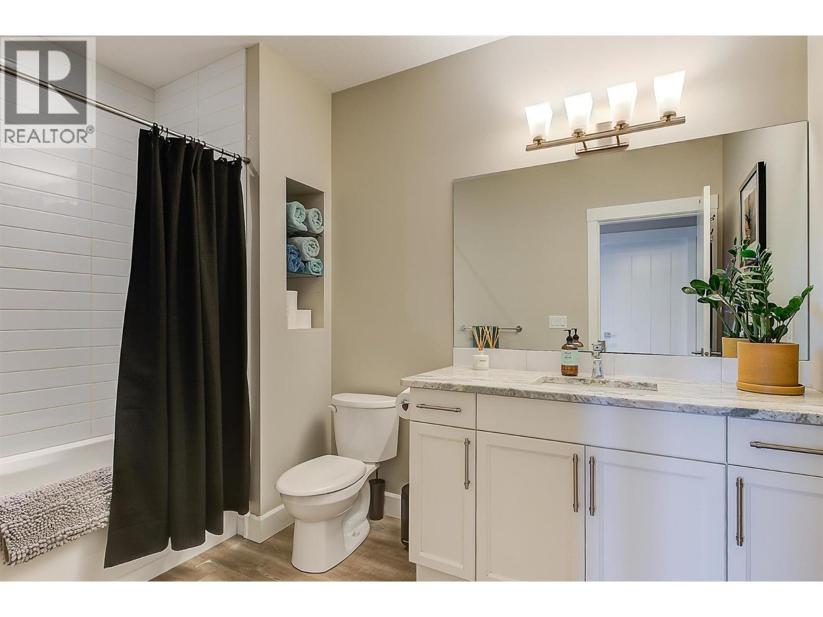 The four-piece bathroom features a tub/shower combo, white tile, quartz countertops, a large mirror and white cabinetry. - 738 Highpointe Drive, Kelowna, BC - Indoor Photo Showing Bathroom