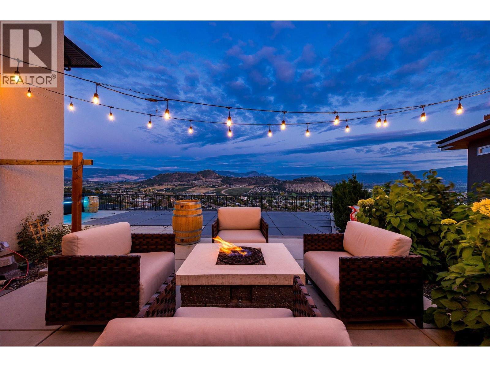 a cozy additional space with a built in fire table (no need for a propane tank) with stylish wooden fencing and hedges. - 738 Highpointe Drive, Kelowna, BC - Outdoor With Deck Patio Veranda