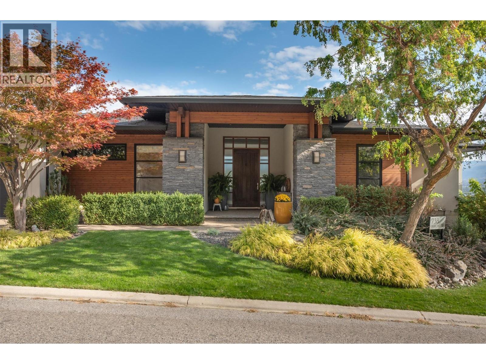 The front yard showcases mature landscaping along the side and front of the house including a small grassy area. Truly a low-maintenance design requiring minimal mowing - 738 Highpointe Drive, Kelowna, BC - Outdoor